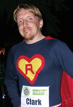 A beautiful redheaded man wearing superman clothes and a sticker that says Clark.
